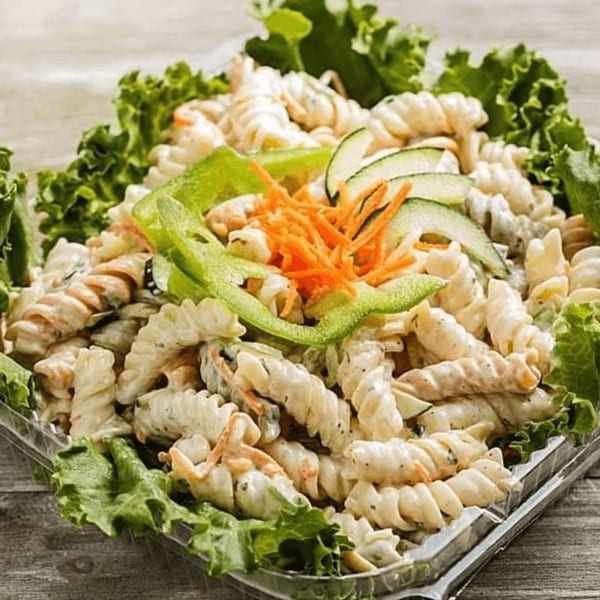 Creamy pasta salad with spiral pasta, shredded carrots, cucumber, and green bell pepper, garnished with lettuce.