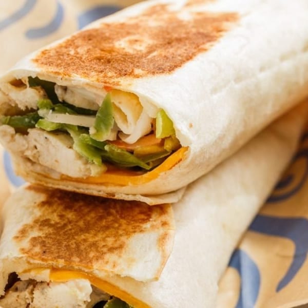 Two Roly Poly wraps, filled with chicken, cheese, and lettuce, stacked on a patterned surface.