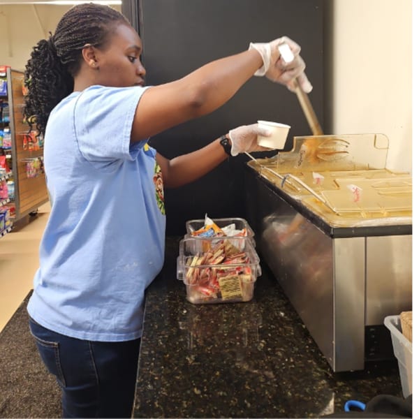 A woman in a light blue shirt and gloves serves food from a buffet line.