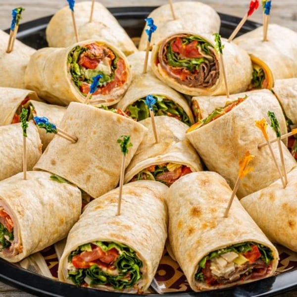A platter of Roly Poly wraps, cut in half and secured with colorful toothpicks, showcasing fresh ingredients.