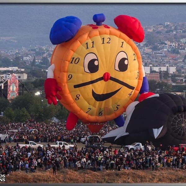 A giant Roly Poly alarm clock hot air balloon floats above a crowd of people.