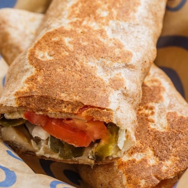 Close-up of a Roly Poly sandwich, revealing tomatoes, pickles, and onions inside a toasted wrap.