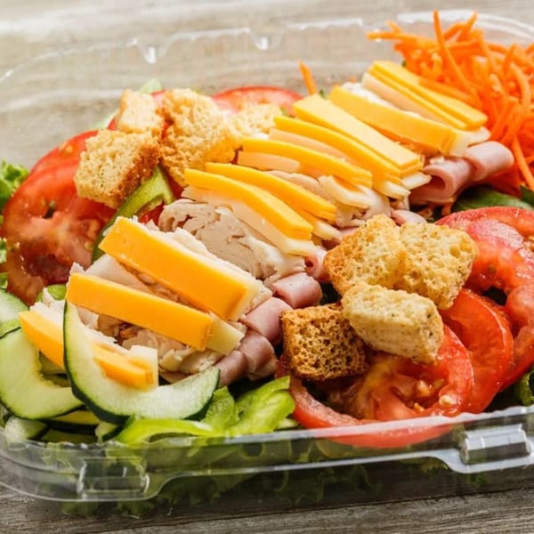 A Roly Poly chef salad with ham, turkey, cheese, croutons, and vegetables in a plastic container.