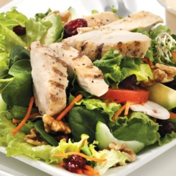 Grilled chicken salad with mixed greens, cranberries, walnuts, and sliced vegetables.