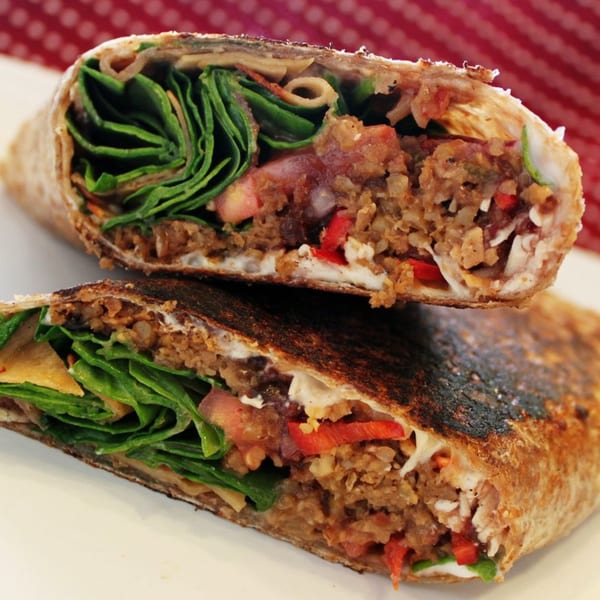Two halves of a Roly Poly wrap, filled with meat, spinach, tomatoes, and cheese.