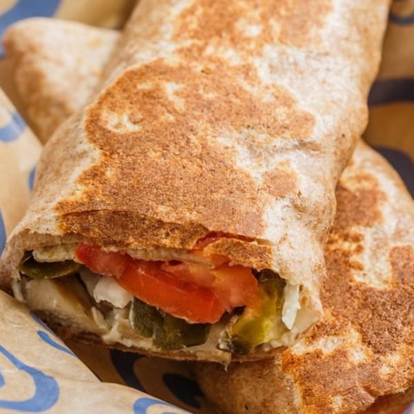 A Roly Poly sandwich wrap, cut in half, revealing tomatoes, pickles, and white sauce.