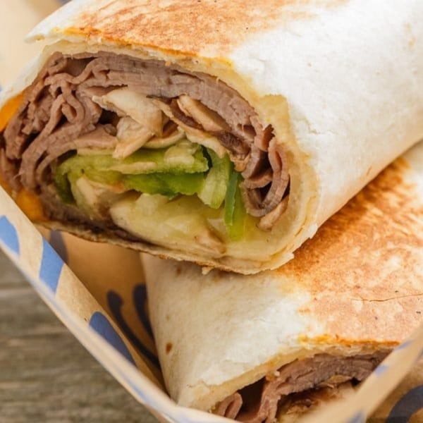 Close-up of a Roly Poly wrap, filled with sliced meat, lettuce, and cheese, in a paper holder.