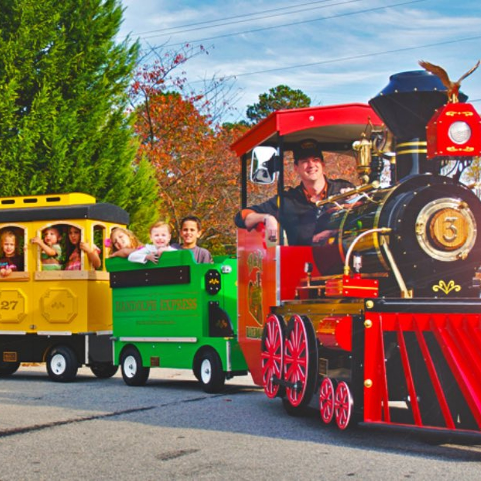 A conductor drives a colorful Roly Poly Express train with children waving from the passenger cars.