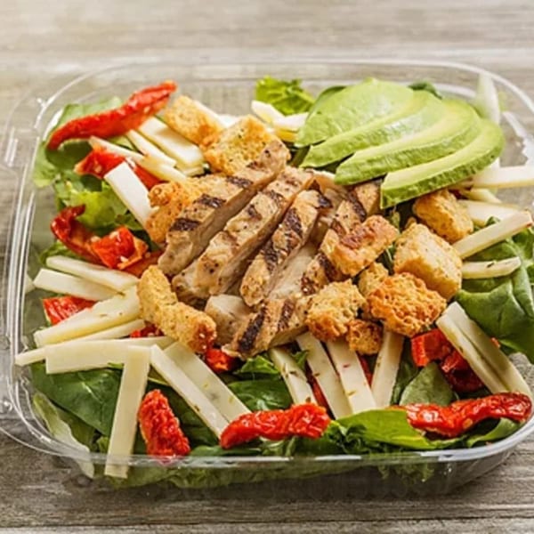 Roly Poly's grilled chicken salad with avocado, croutons, cheese, and sun-dried tomatoes in a plastic container.