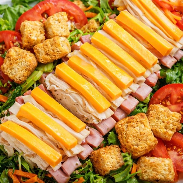 A vibrant Roly Poly chef salad with ham, turkey, cheese sticks, croutons, and tomatoes.