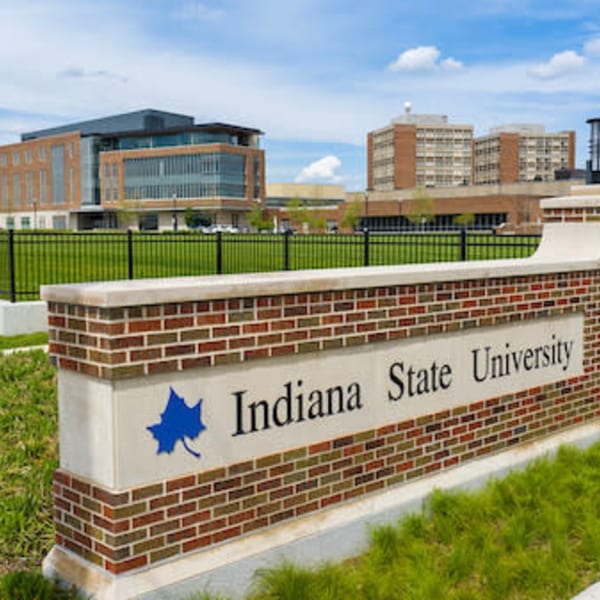 Brick sign for Indiana State University with campus buildings and a blue sky in the background.