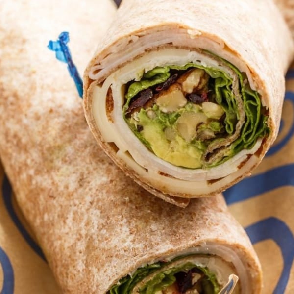 Two Roly Poly wraps, one cut in half, revealing turkey, cheese, avocado, and lettuce.