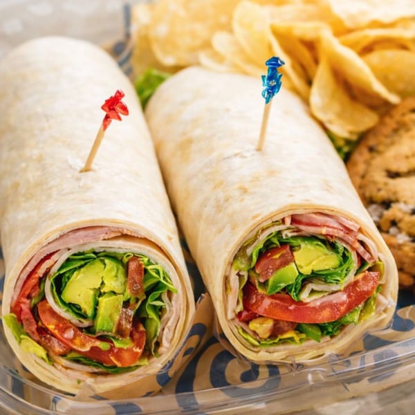 Two Roly Poly wraps filled with meat, avocado, tomato, and lettuce, served with chips and a cookie.