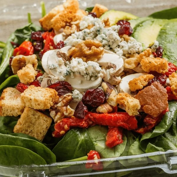 A vibrant Roly Poly salad with spinach, mushrooms, blue cheese, cranberries, walnuts, and croutons.