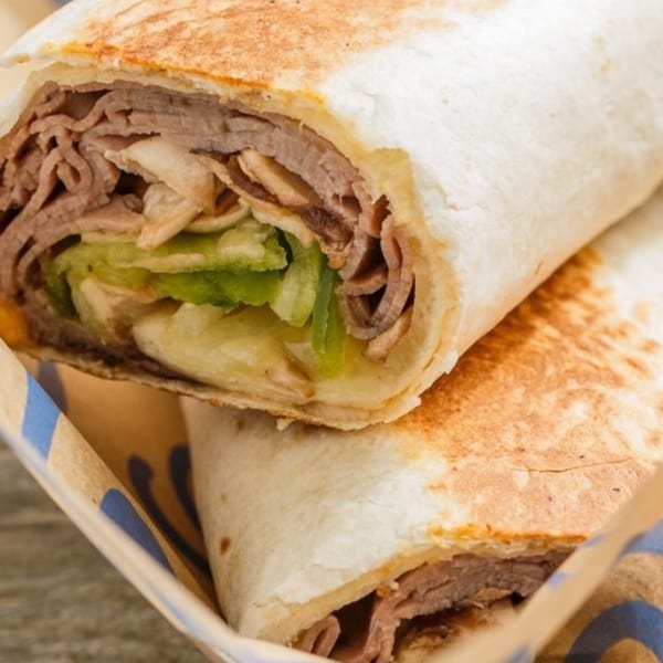 Two Roly Poly roast beef wraps with lettuce and cheese in a branded paper holder.