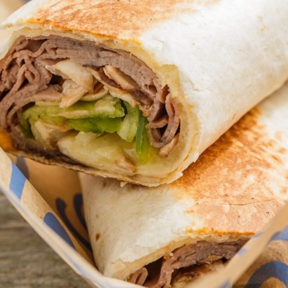 Two Roly Poly roast beef wraps with lettuce and cheese in a branded paper holder.