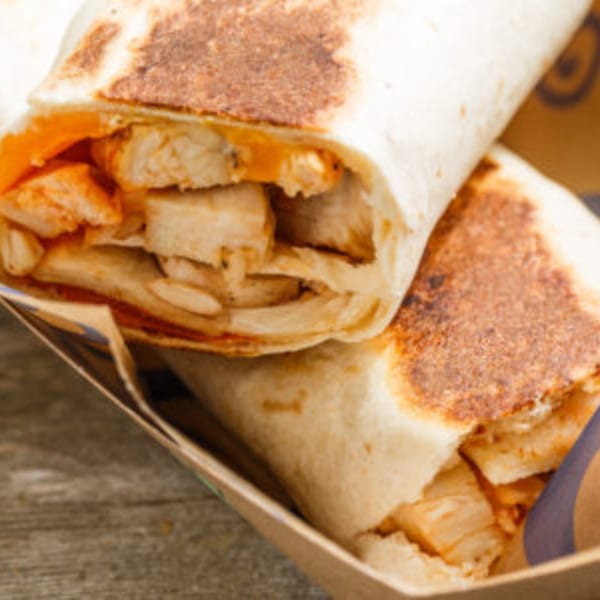 Two Roly Poly sandwiches, filled with chicken and sauce, in a brown paper holder.