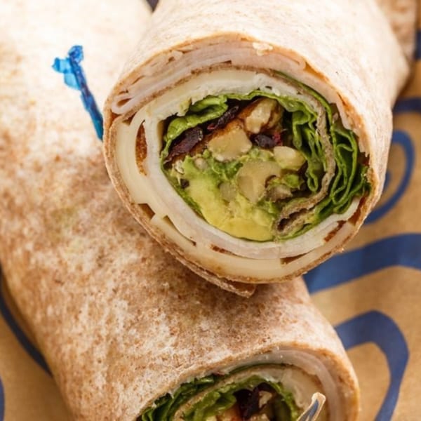 Two Roly Poly wraps, one cut in half, revealing turkey, avocado, lettuce, and cheese.